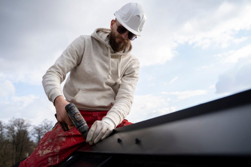 A man on the roof using his tools doing emergency roofing services.